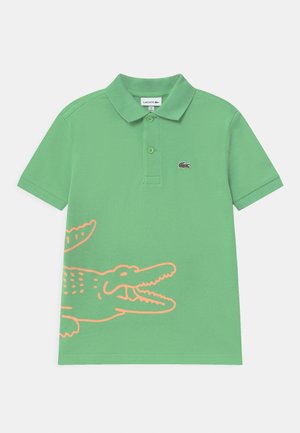 Groen poloshirt met korte mouwen, kraag, twee knopen, klein Lacoste krokodillenlogo op de borst en groot oranje omrande krokodillendesign onderaan.