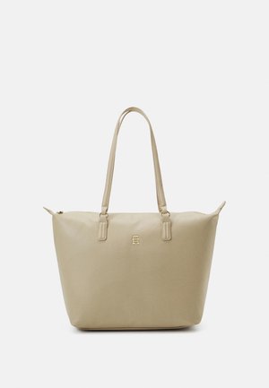 Sac fourre-tout beige fabriqué en matériau synthétique lisse, avec deux longues poignées, quincaillerie dorée et un accent logo sur le devant.