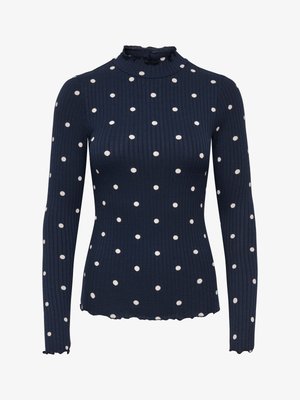 Navy ribgebreide coltrui met lange mouwen, voorzien van witte stippen en een gerimpelde halslijn. Golvende zoomdetails zorgen voor textuur.