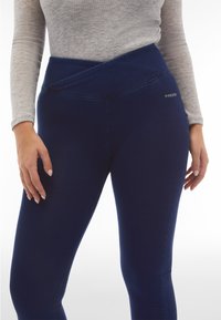 Leggings a vita alta di colore blu navy con un design della vita asimmetrico, realizzati in materiale elasticizzato. Presentano un logo discreto sull'anca.