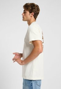Roomkleurige katoenen t-shirt met korte mouwen, voorzien van een bruin grafisch ontwerp op de achterkant en een relaxte pasvorm.