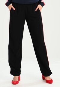 Svarta träningsbyxor med röda sidestreck, elastisk midja och fickor. Slät fabrik med en avslappnad, rak ben-design.