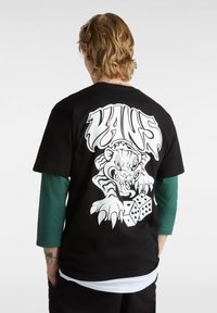 Camiseta negra con un gran gráfico blanco de un tigre y dados en la parte posterior. Manga corta, material de algodón y diseño de cuello redondo.