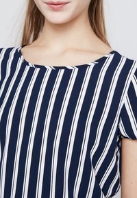 Marineblauwe top met horizontale witte strepen, ronde halslijn, korte mouwen, gladde stofstructuur en een ontspannen pasvorm.