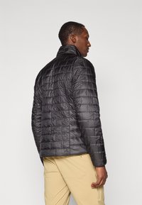 Veste doudoune noire avec un design matelassé, col montant et finition texturée. Présente une coupe slim et est montrée de dos.