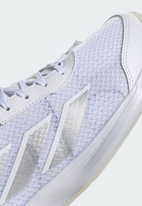 Bílé atletické boty s texturovaným textilem, metalickými stříbrnými akcenty a gumovou podrážkou; disponují klasickými tkaničkami a polstrovaným límcem.
