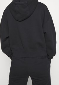 Zwarte cropped hoodie gemaakt van een zachte katoenmix, met een capuchon met trekkoord, brede mouwen, zichtbare naaddetails en een ontspannen pasvorm.