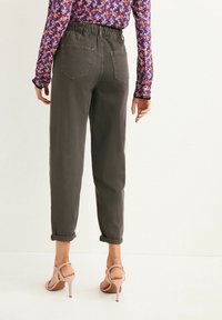 Pantaloni grigi con vita elasticizzata e vestibilità comoda, con le maniche bordate, abbinati a sandali con tacco alto beige. La parte superiore presenta un motivo floreale.