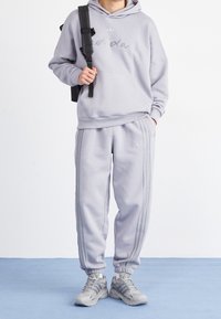 Grå hoodie och sweatpants-set med tre ränder längs sidorna, med en framficka och subtil logga.