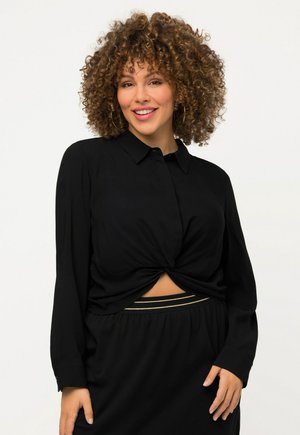 Chemise noire à manches longues avec un design noué à l'avant et une texture lisse, associée à une jupe noire avec des accents dorés.