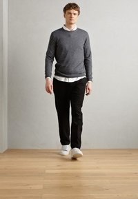 Sueter gris, camisa blanca con cuello, pantalones negros y zapatos blancos. La tela parece suave, con un diseño ajustado, sobre un fondo de suelo de madera.