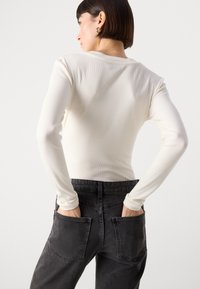 Haut à manches longues en maille côtelée de couleur crème associé à un jean en denim noir taille haute avec de grandes poches arrière. Texture lisse sur l'ensemble.