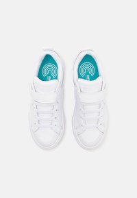 Baskets blanches avec un dessus synthétique lisse, dotées d'une sangle Velcro, de lacets et d'une semelle intérieure bleu canard vive avec des motifs circulaires.