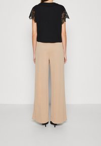 Top corto negro con mangas de encaje combinado con pantalones anchos beige. El conjunto presenta un ajuste holgado y texturas suaves.