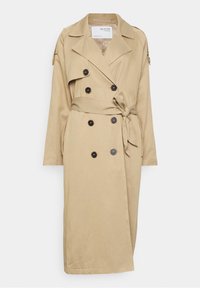 Beżowy trencz o podwójnym zapięciu, z dużymi czarnymi guzikami, bocznym paskiem do związania i pagonami na ramionach. Miękka faktura materiału.