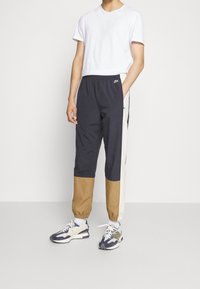 Námořnicky modré a béžové teplákové kalhoty s elastickým pasem, zužující se spodní částí a kontrastním světle hnědým panelem. Kombinované s jednobarevným bílým tričkem a teniskami.