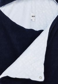 Couche extérieure en tissu côtelé bleu marine avec une doublure à motif blanc. Dispose d'un détail de fermeture à bouton, étiqueté "BOSS" à l'intérieur.