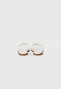 Sandale plate albe cu un design minimalist, prezentând o curea subțire și o talpă bej deschis. Textură netedă, spate deschis și fără accente suplimentare.
