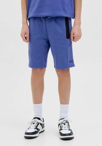 Pantaloni corta blu con tasca laterale con zip, vita elastica e polsini a costine. Abbinati a sneaker nere e bianche.