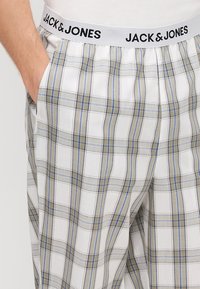 Vita rutiga pyjamasbyxor med blå och grå rutig mönstring, med en mjuk midja märkt "JACK & JONES." Lättviktsmaterial, avslappnad passform.