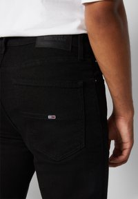 Vaqueros de denim negro con un diseño de pierna recta, que cuentan con un bolsillo trasero acentuado por un pequeño parche de logo de marca y costuras en contraste.
