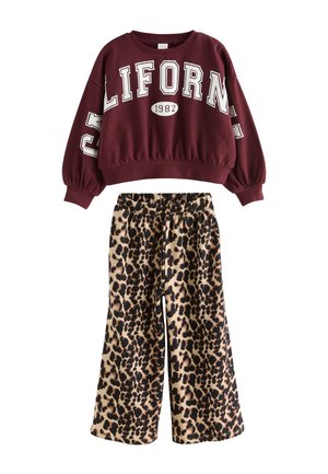 Bordowa krótka bluza z napisem "CALIFORNIA 1982" w połączeniu z szerokimi spodniami o beżowo-czarnym wzorze w cętki.