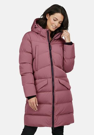 Vrouw die een lange, mauve donsjas met kap draagt, met een rits aan de voorkant en klepzakken, haar haar aanraakt en glimlacht met gesloten ogen.
