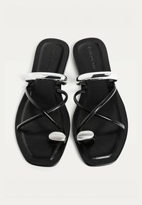 Svarta platta sandaler med en snygg design, med tvinnade remmar, en glänsande kromdetalj och en fyrkantig tåform. Slät yta överlag.