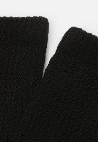 Schwarze Strumpfsocken mit gerippter Textur, entworfen aus einem glatten, weichen Material und mit einer engen Passform. Die Kanten sind ordentlich verarbeitet.