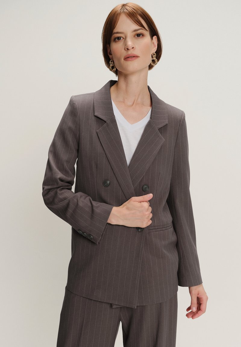 Grijze streepjes dubbele blazer met zwarte knopen, getailored fit, met geknipte revers en details van de voorzak, gedragen over een wit T-shirt.