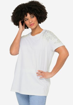 Camiseta blanca de tejido suave con embellishments en plata decorativos en los hombros. Mangas cortas y corte holgado.