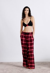 Μαύρο μπραλέτ με κόκκινη λεπτομέρεια συνδυασμένο με άνετο παντελόνι πυτζάμας σε κόκκινο και μαύρο καρό. Μαλακή υφή, φαρδιά πόδια και λάστιχο με κορδόνι στη μέση.