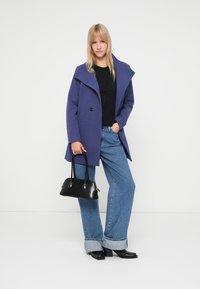 Purple wool blend coat with a wide collar and two buttons, paired with a black top, light blue wide-leg jeans, and a black handbag.