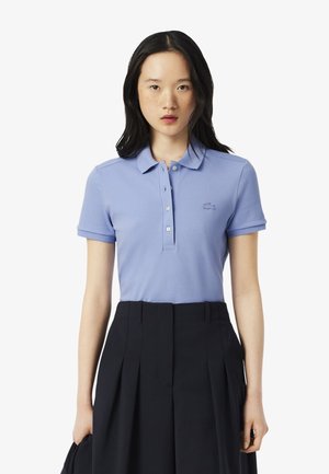 Polo shirt azzurro chiaro con colletto, apertura a tre bottoni e logo ricamato. Abbinato a pantaloni a vita alta neri plissettati.