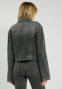 Szara, dżinsowa kurtka w kroju cropped z klasycznym kołnierzykiem, długimi rękawami i detalami przeszycia. Materiał ma wyblakłą teksturę oraz dobrze zdefiniowany kształt.