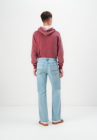 Rdeča kapuca siva podloga, kombinirana z svetlo modrimi jeans hlačami ravnega kroja. Hlače imajo zadnje žepe in klasičen denim videz.