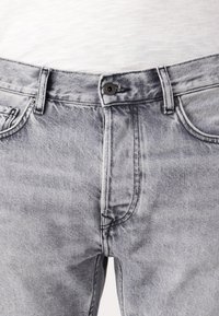 Graue Jeans aus Denim mit einem verwaschenen Finish, ausgestattet mit einem Knopfverschluss, vorderen Taschen und kontrastierenden Nähdetails.