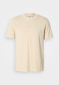 Light beige cotton t-shirt with a round neckline and short sleeves. Features subtle printed branding on the chest. Smooth texture.