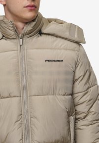 Bežna napihnjena jakna izdelana iz sijoče tkanine, z sprednjim zadrgo, oversized ovratnikom in črnim logotipom "PAGADOR" na prsih.