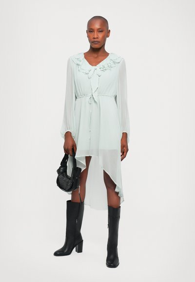 Rochie mint-verde deschis, cu guler ruffled, mâneci lungi și tiv asimetric. Purtați cu cizme negre până la genunchi și o geantă de mână mică, neagră.
