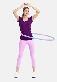 Purple athletic t-shirt and pink leggings. A multicolored hula hoop is around the waist. Model is wearing white training shoes.