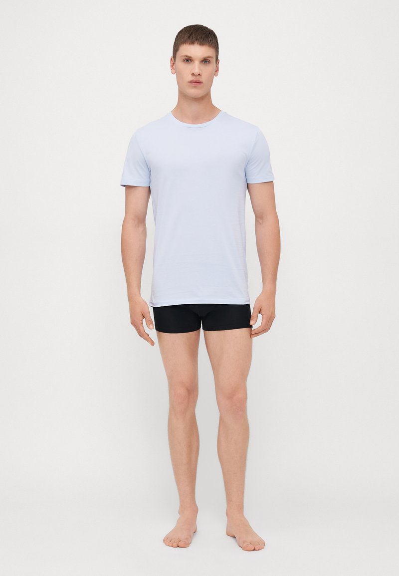 Šviesiai mėlyna trumpa rankovė t-shirt, pagaminta iš minkštos medžiagos, derinama su juodais šortais. T-shirt turi apvalų kaklą ir prigludusią formą.