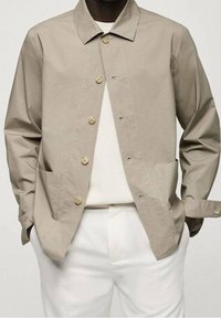 Giacca button-up di un beige chiaro realizzata in tessuto liscio, con due tasche frontali, un colletto classico e un fit rilassato.