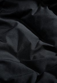 Tessuto di raso nero con una texture liscia e lucida, che mostra morbide pieghe fluide e sottili riflessi di luce sulla sua superficie.