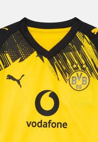 Maillot de sport jaune avec des accents noirs, col en V, présentant des motifs géométriques, logo Puma, logo Vodafone et emblème du club BVB 09.