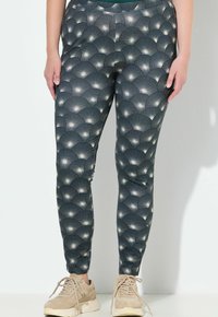 Strak zittende legging gemaakt van rekbare stof, met een donkere achtergrond en een herhalend waaierpatroon in lichtgrijs en witte accenten.