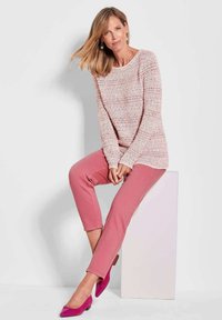 Texturiertes Strickpullover in sanften Farben, kombiniert mit rosa Hosen. Die Accessoires umfassen rosa High Heels, einfache Ohrringe und eine natürliche Frisur.