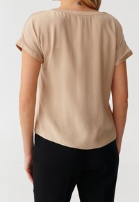 Beige krátký rukáv top s hladkou texturou, kulatým výstřihem a mírně zakřiveným lemem, doplněný jednoduchým a čistým designem.