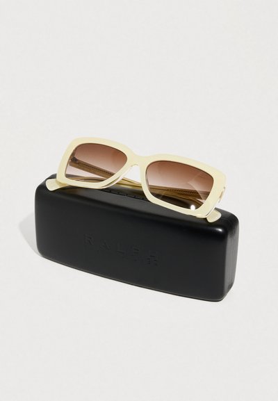 Γυαλιά ηλίου με πλαίσιο σε απαλό κίτρινο χρώμα και βαθμιαία καφέ φακούς, τοποθετημένα σε ματ μαύρη θήκη με ανάγλυφο λογότυπο.