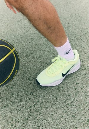 Fényes sárga Nike sportcipő fekete részletekkel, légáteresztő hálós felsőrésszel és texturált talppal, egy kosárlabda mellett egy pályán.